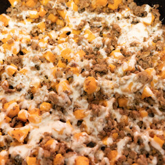 Ground turkey meat, cubed sweet potatoes, melted mozzarella cheese, and diced onions served for dinner in a cheesy, nutritious cast iron skillet meal in a home kitchen.
