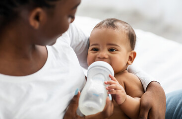 African American woman feeding her child from baby bottle - Powered by Adobe