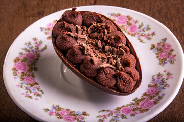 Mini stuffed chocolate easter egg with grated chocolate on the top on a white plate with flowers design on a wooden table.