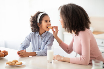 Cheerful african american woman feeding girl with cookie