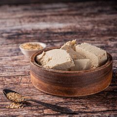 Pieces of tahini halva in a bowl on vintage wooden background, with sesame seeds as its main ingredient