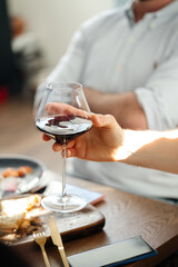 A glass of red dry wine in the hand of a handsome man against the background of a table and dinner with friends. Understand the toast.