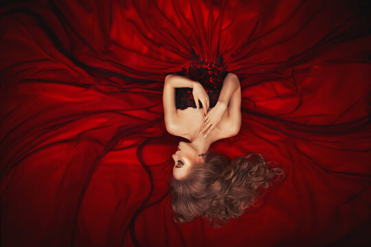 Portrait of a reclining beautiful blonde girl in a dark red ball gown