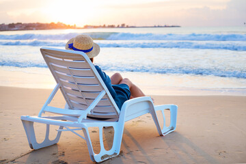 Obraz premium Beautiful girl in a hat sits on a deckchair meeting the dawn