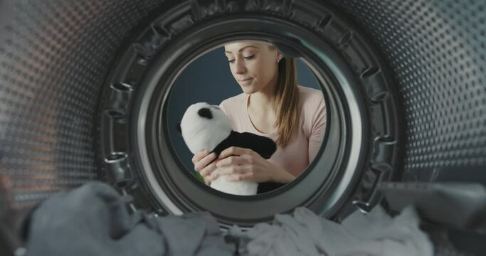 Woman opens the washing machine door and takes a freshly washed plushie, she is happy and hugs it