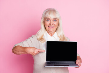 Fototapeta premium Photo of old woman hold netbook direct finger display empty space wear beige cardigan isolated pastel pink color background