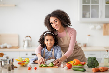 Cheerful black mom teaching daughter how to prepare salad