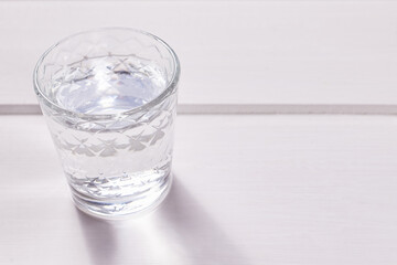 A faceted shot glass of vodka on a white wooden background.