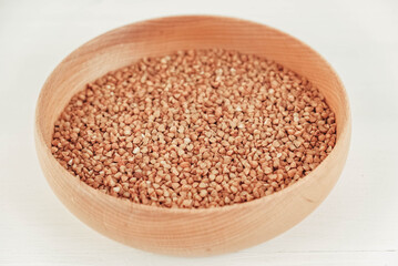 Buckwheat kernels in wooden bowl on white background. Top view. Copy, empty space for text