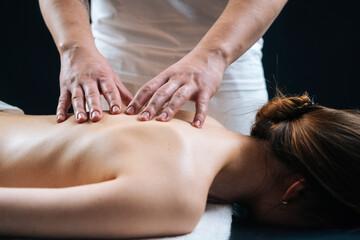 Close-up hands of male masseur doing back massage to young relaxed woman lying in massage table at...