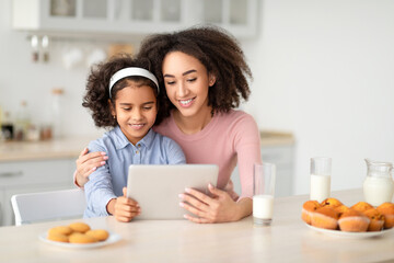 Black mother and daughter using tablet looking for new recipes