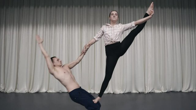 An acrobatic duo rehearses on stage. Young gymnasts do acrobatic stunts. Choreographic movements. The guy and the girl go in for sports. Strength and exercise.Dramatic performance of acrobats on stage