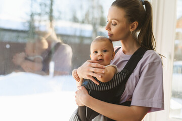 A young mother with a child in her arms stands by the window. Happy family. Motherhood during quarantine. Home insulation