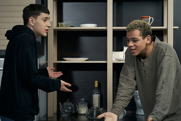 Staged photo illustrates problems and conflicts in gay couple relationships. Two young men are in the moment of showdown in the kitchen. Partners are emotional and proving something to each other.