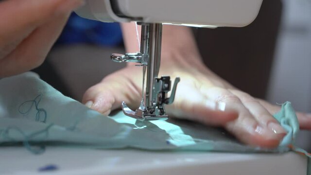 Tailor repairs or makes new clothes using professional sewing machine, close up, top view. Person stitches border seam on the edge of fabric and checks it.