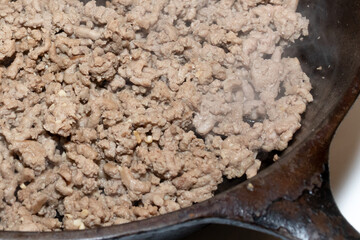 Ground turkey meat cooking in a cast iron skillet on a stove top in a home kitchen.