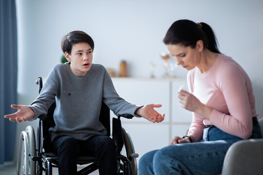 Family Disagreement. Upset Mother Crying And Her Teenage Son In Wheelchair Trying To Justify Himself At Home