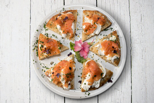 Pizza with salmon and mozzarella burrata cheese, six slices in white plate on white wooden boards background, flat lay in top view