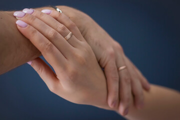 A loving couple holding hands. Against a dark background. And wedding rings on my hands.