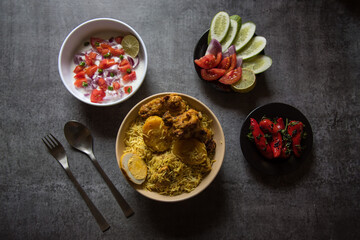 Top view of  piece of boiled egg on chicken biryani or traditional rice along with potato in a bowl and condiments