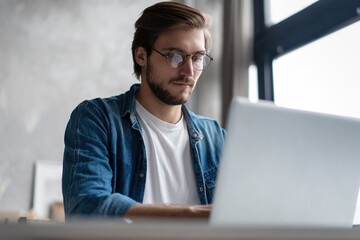 Young man freelancer using laptop studying online working from home, happy casual guy typing on notebook