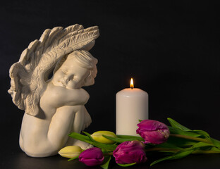 Lonely angel with a white burning candle and tulip flowers as a symbol of death and the end of...