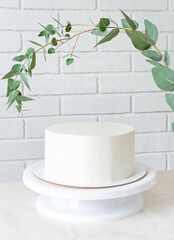 white cake without decor on a stand under a sprig of eucalyptus. cake with copy space