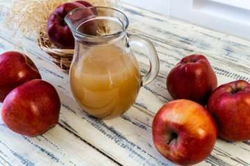 Red apples in a basket and apple juice in a jug on a wooden table