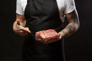 Closeup a man butcher wearing black apron pointing finger to raw pork rib. Mockup, place for text.