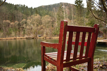Roter Lehnstuhl vor Fischteich im Wald im Winter, Frühling