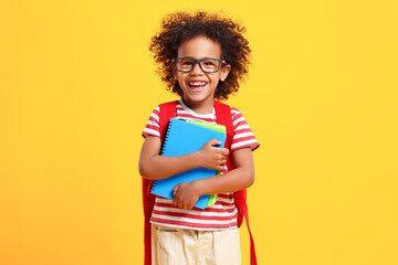 Happy schoolkid laughs at camera standing in studio with copybooks in hands