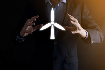 Businessman holding an icon of a windmill that produces environmental energy. Dark background