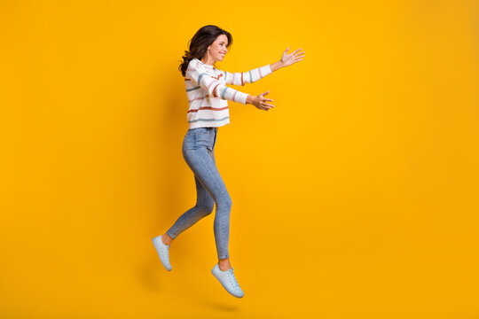 Full size profile side photo of happy excited smiling girl jumping open hands hug embrace isolated on yellow color background