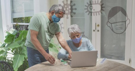Animation of covid 19 icons over senior couple using laptop wearing face masks - Powered by Adobe