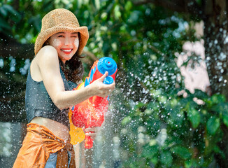 Smiling Asian woman was splashed by water. She is using a water gun for Songkran Festival.