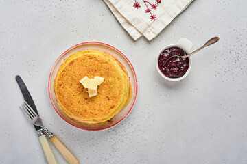 Crepes or thin pancakes stack with butter and raspberry jam on beautiful ceramic plate on an old gray concrete background. Top view, copy space. Homemade thin crepes for breakfast or dessert.