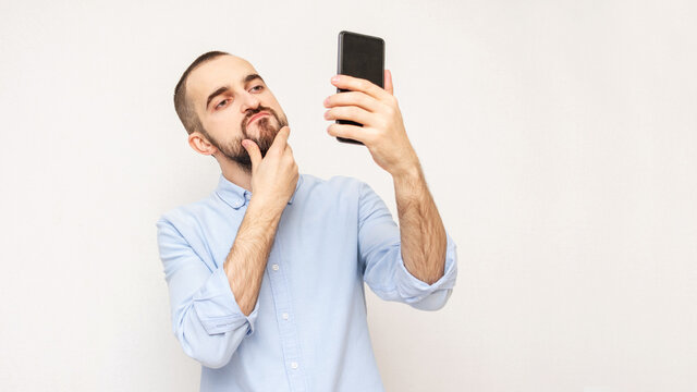 Narcissistic bearded takes a selfie with smartphone, white background, copy space, 16:9
