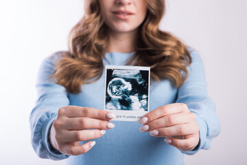 Portrait of a pregnant girl with an ultrasound scan in her hands in the studio on a white background