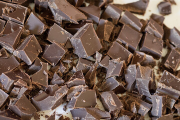 Chopped chocolate pieces on a white cutting board in a domestic kitchen to be used as an ingredient in a recipe.