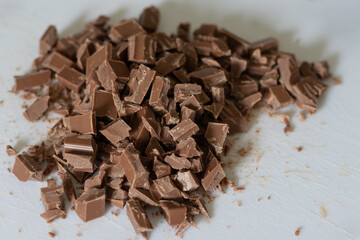 Chopped chocolate pieces on a white cutting board in a domestic kitchen to be used as an ingredient in a recipe.