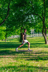 Sporty young man stretching legs and doing forward lunge while having workout at the park