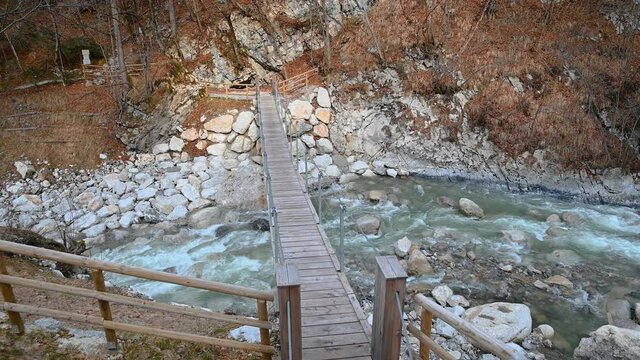 Elevated view of clean Alpine river flowing in narrow Dovzan gorge, Slovenia. Small suspension bridge over turbulent stream. Pristine nature in the Alps. Static shot, real time