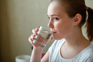Young woman drinks glass of pure water in morning after waking up. Happy teen girl maintains water balance for body health by drinking a transparent cup of clean water.
