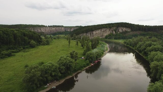 Camping tourists with tent after catamaran relax rafting cruise on mountain river in Ural Mountains. Group of people engaged wild leisure relaxation. Aerial view drone wide view at summer sunny day