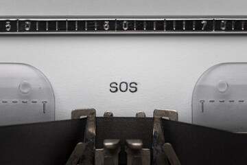 Typing text SOS on vintage manual typewriter. Close up of writes word on white paper. Typing a...
