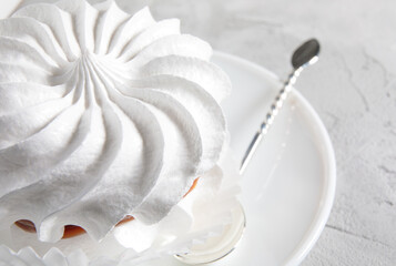 Beautiful white meringue with a silver spoon on a white plate. White cake.
