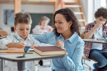 Happy kind teacher is helping kids in elementary school lessons