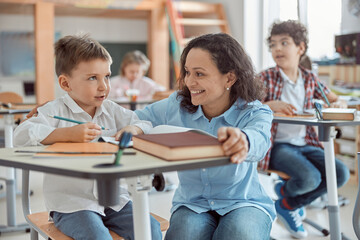 Happy kind teacher is helping a boy in elementary school lessons