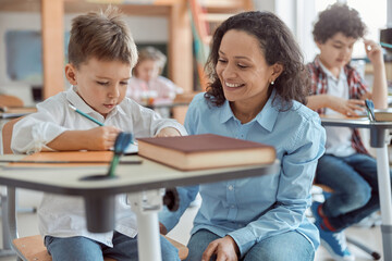 Happy kind teacher is helping a boy in elementary school lessons