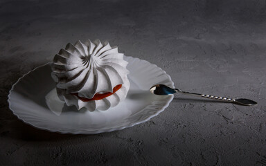 Beautiful white bezé with a silver spoon on a white plate. White cake. concrete background.